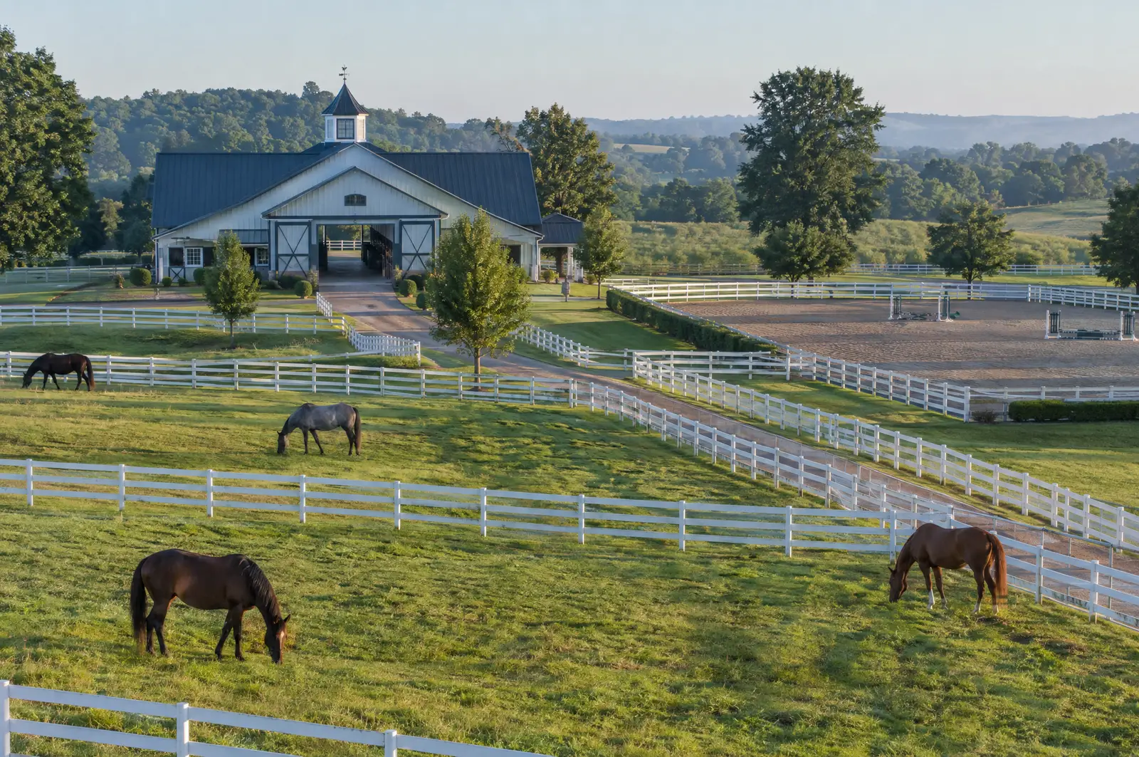Horse farm with white board fences, grazing horses, a center-aisle barn and riding arena