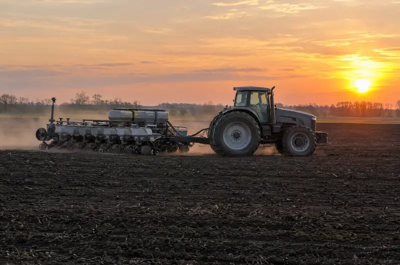 Tractor pulling a row-crop planter across a field at sunrise