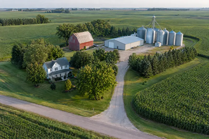 Aerial view of a family farmstead with farmhouse, red barn, machine shed and grain bins