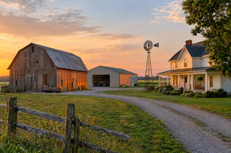 Old wooden barn, machine shed and farmhouse on a family farm at sunset